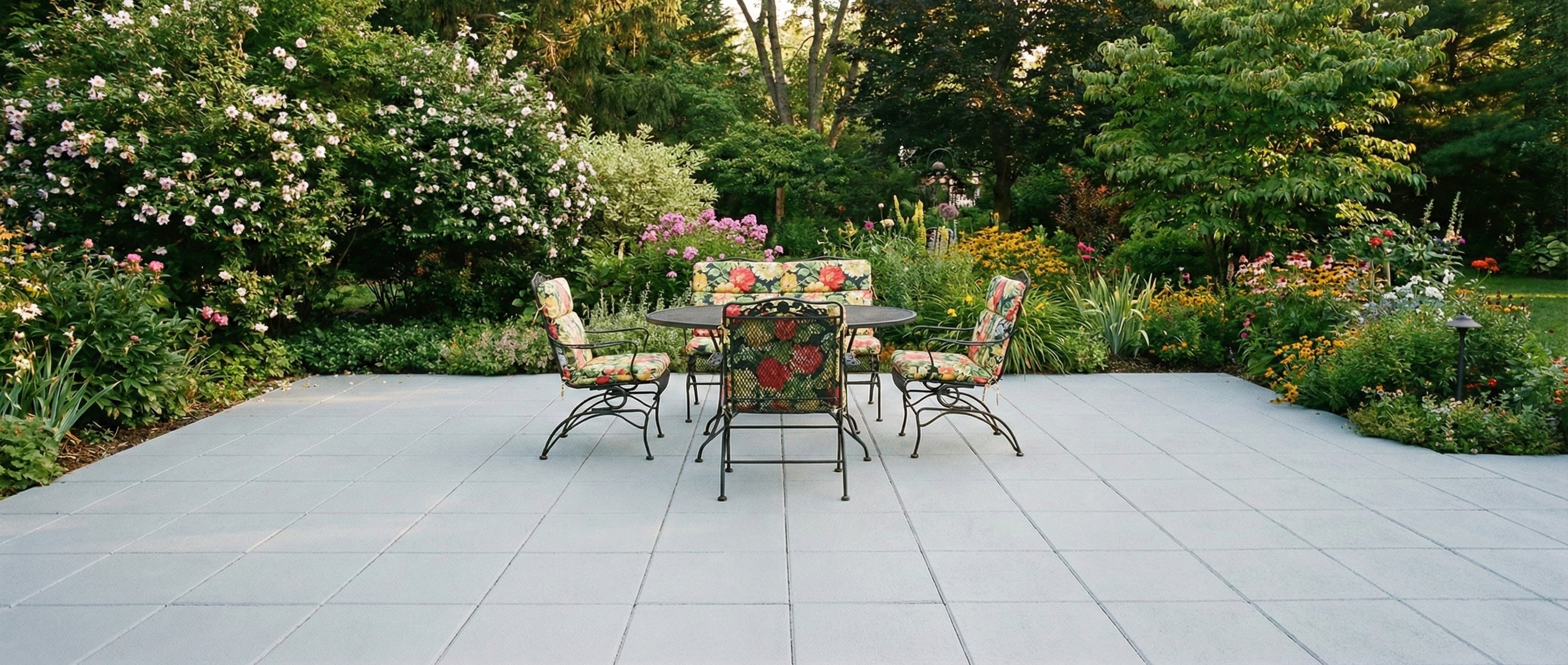Outdoor patio set with table and chairs on a concrete patio surrounded by garden plants.
